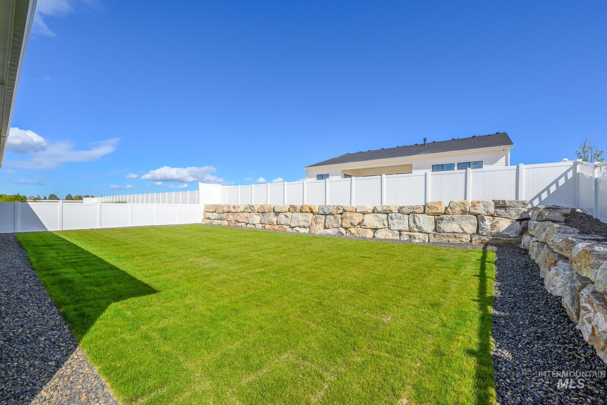 14676 Serenity Pt Street Caldwell, ID 83607 - Photo 32 of 41 Expansive backyard featuring a manicured lawn, full white privacy fencing, and robust stone retaining walls