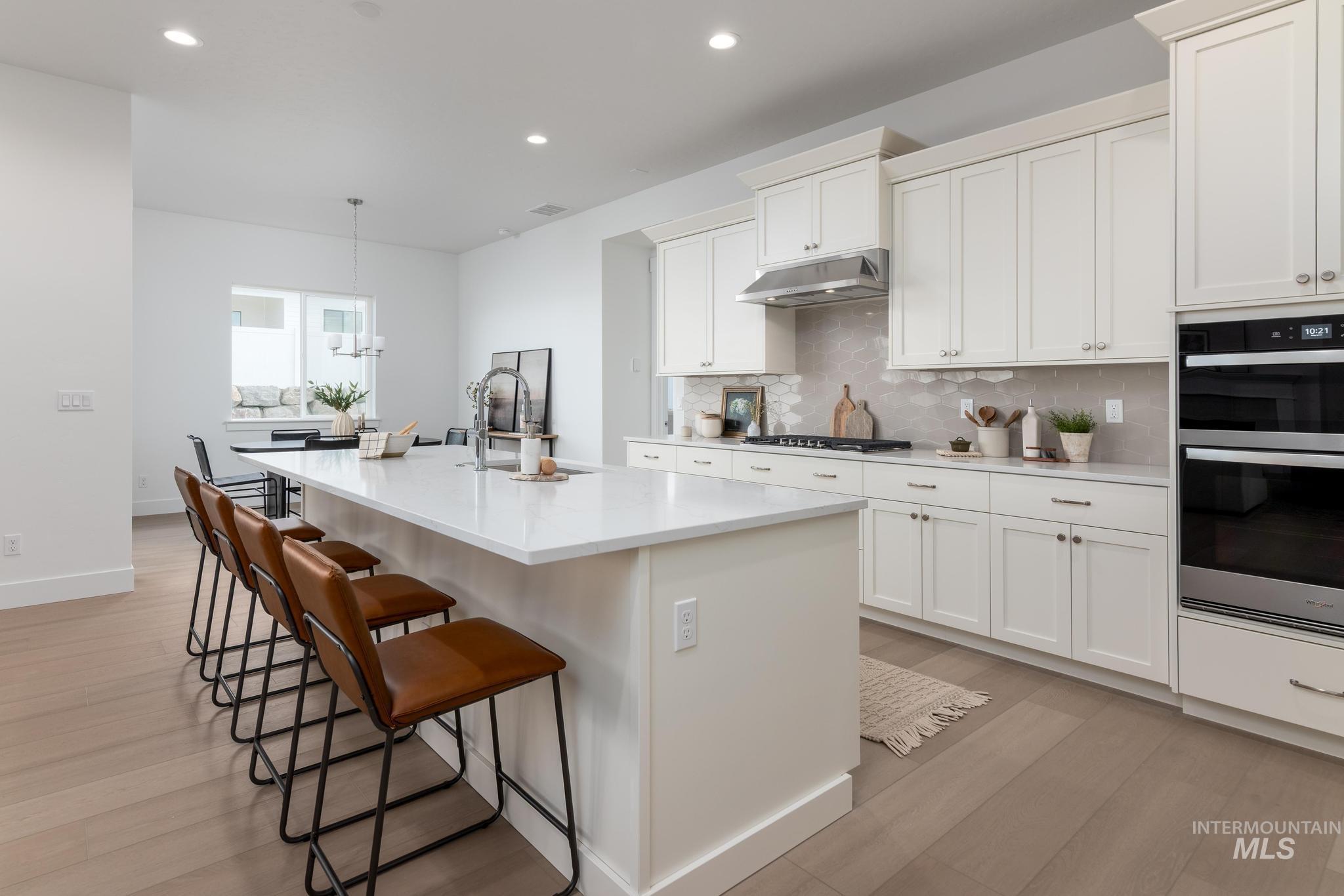 14676 Serenity Pt Street Caldwell, ID 83607 - Photo 9 of 41 Kitchen featuring an expansive island with seating, integrated sink with gooseneck faucet, light-toned wood-finish flooring, white shaker-style cabinetry with crown molding, and stainless steel double wall ovens