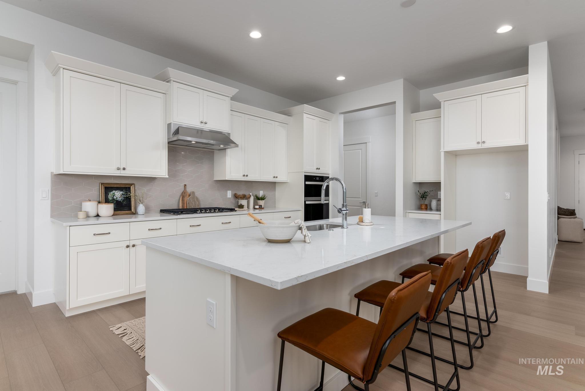 14676 Serenity Pt Street Caldwell, ID 83607 - Photo 10 of 41 Gourmet kitchen featuring white shaker cabinetry, an expansive center island with seating, integrated double ovens, a gas cooktop with a stainless steel range hood, and wood-finish flooring