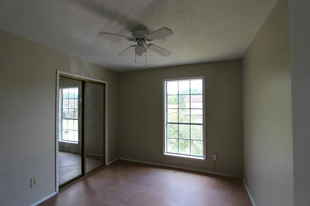 an empty room with chandelier fan and windows