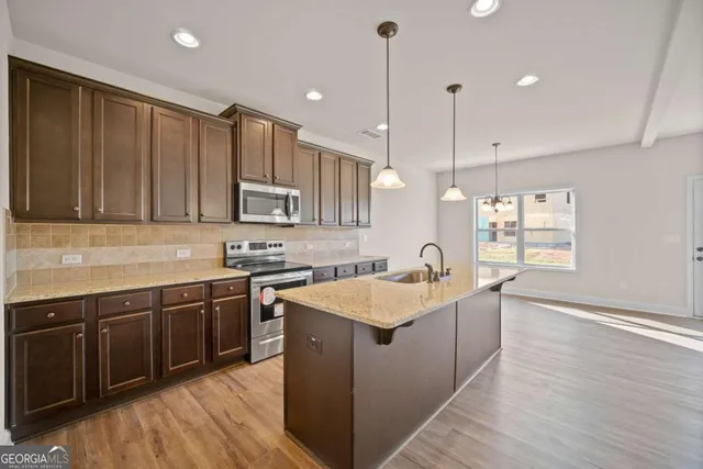 a kitchen with stainless steel appliances granite countertop wooden cabinets a sink dishwasher a stove and a refrigerator with wooden floor