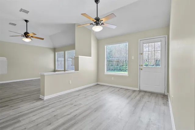 an empty room with wooden floor chandelier fan and windows