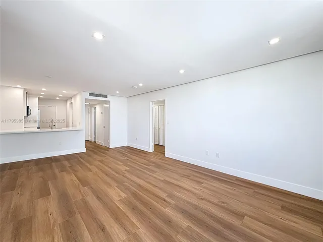 a view of an empty room with wooden floor and a kitchen