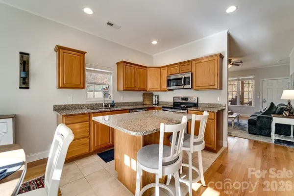 a kitchen with stainless steel appliances granite countertop a stove top oven a sink a dining table and chairs with wooden floor
