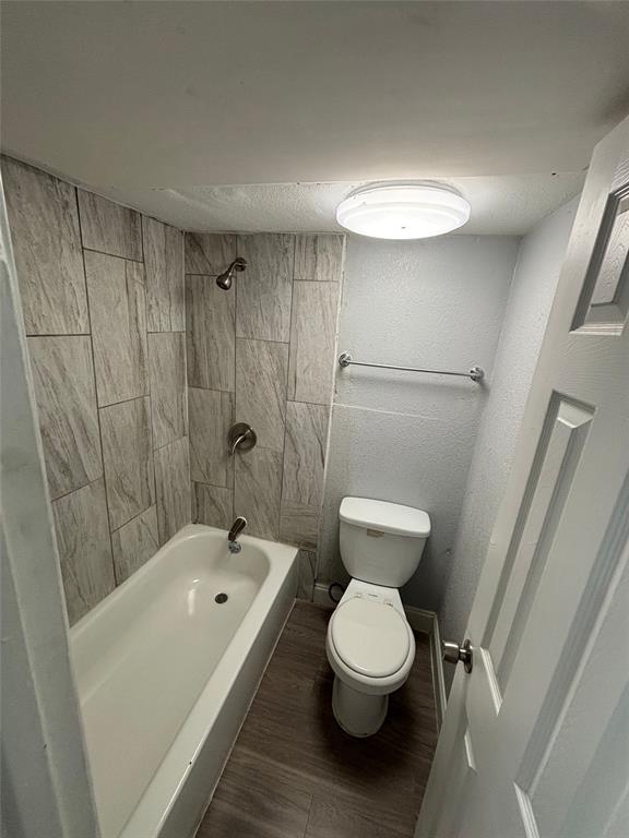 301 Rolston Road, Unit 315101 Irving, TX 75060 - Photo 5 of 12 Bathroom featuring a white bathtub, tiled shower surround with brushed nickel fixtures, a white toilet, and wood-finish flooring