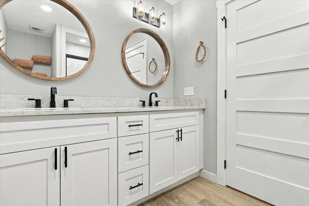 12 Hoot Loop Cartwright, OK 74731 - Photo 15 of 35 Dual vanity with white cabinetry, matte black fixtures, round wood-frame mirrors, and a light-toned countertop