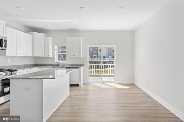 a kitchen with granite countertop a stove a sink and white cabinets with wooden floor
