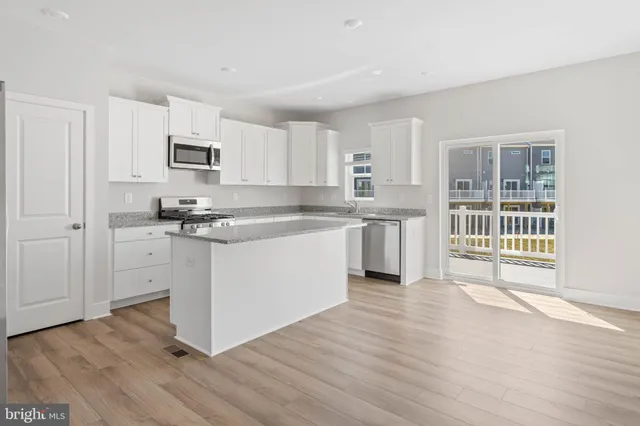 a kitchen with stainless steel appliances a stove top oven a sink a refrigerator white cabinets and wooden floor