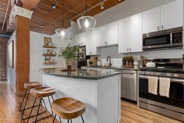 a kitchen with stainless steel appliances granite countertop a sink a stove a microwave a refrigerator cabinets and chairs