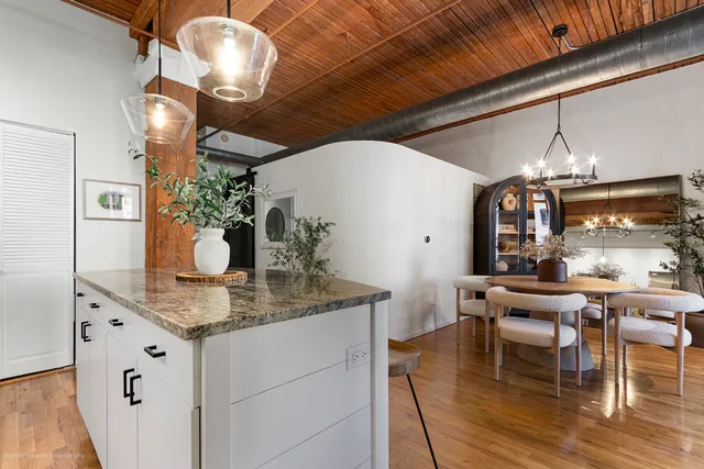 a dining room with kitchen island stainless steel appliances kitchen island granite countertop furniture a chandelier and wooden floor