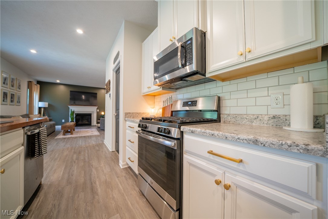 270 Stone Ridge Way Berea, OH 44017 - Photo 14 of 30 Kitchen with white cabinets, light hardwood / wood-style flooring, light stone counters, stainless steel appliances, and decorative backsplash