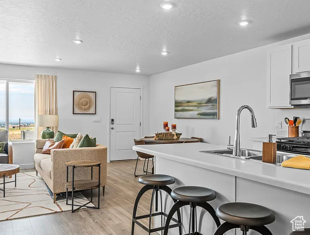 Kitchen featuring light wood-type flooring, stainless steel appliances, sink, a breakfast bar area, and a textured ceiling
