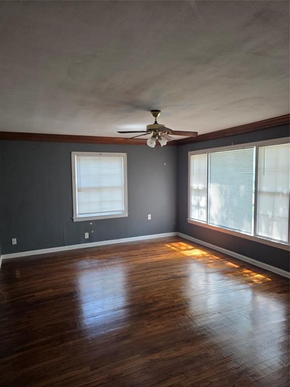 Unfurnished room featuring healthy amount of natural light, ornamental molding, dark wood-style flooring, and a ceiling fan