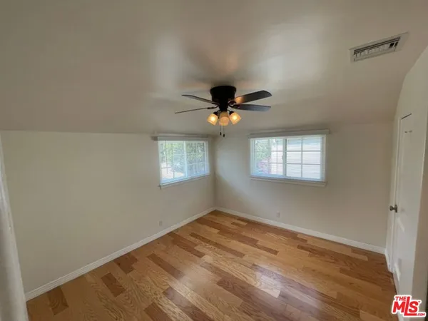 an empty room with wooden floor chandelier fan and windows