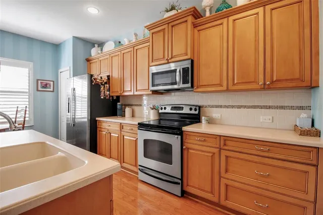 a kitchen with stainless steel appliances a stove top oven a sink a refrigerator a dining table and chairs with wooden floor