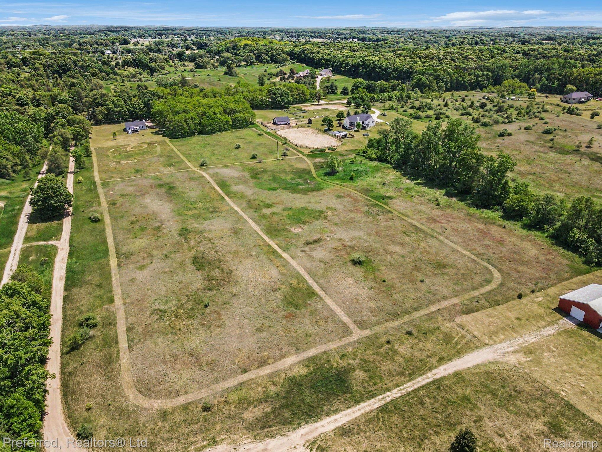 6366 Dutcher Road Howell, MI 48843 - Photo 6 of 33 Expansive rural landscape featuring a large cleared field with visible tracks, bordered by mature trees and verdant foliage
