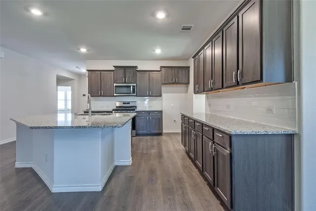 a kitchen with stainless steel appliances granite countertop a stove top oven a sink dishwasher a microwave oven and a refrigerator with wooden floor