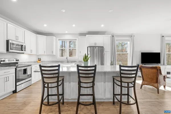 a kitchen with stainless steel appliances a refrigerator a stove a dining table and chairs with wooden floor