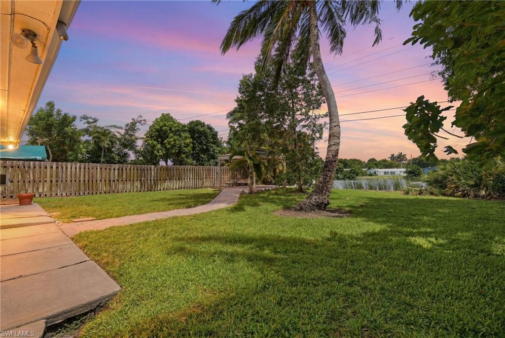 1316 Rordon Avenue Naples, FL 34103 - Photo 29 of 38 Expansive backyard featuring a manicured lawn, a winding paved pathway, a full privacy fence, and mature tropical landscaping