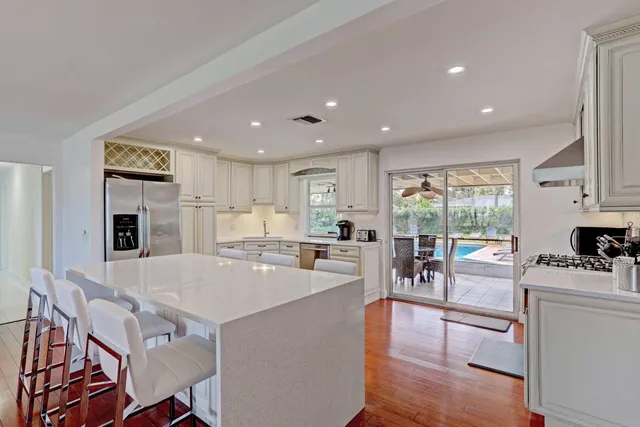 a living room with stainless steel appliances furniture wooden floor and a kitchen view