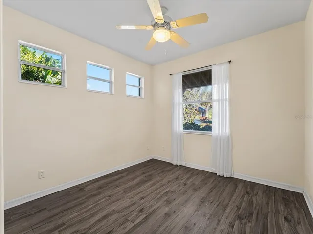 an empty room with wooden floor chandelier fan and windows