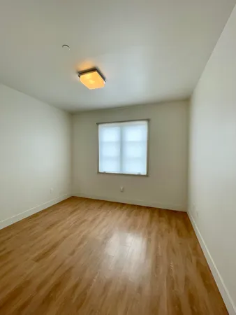 a view of an empty room with wooden floor and a window