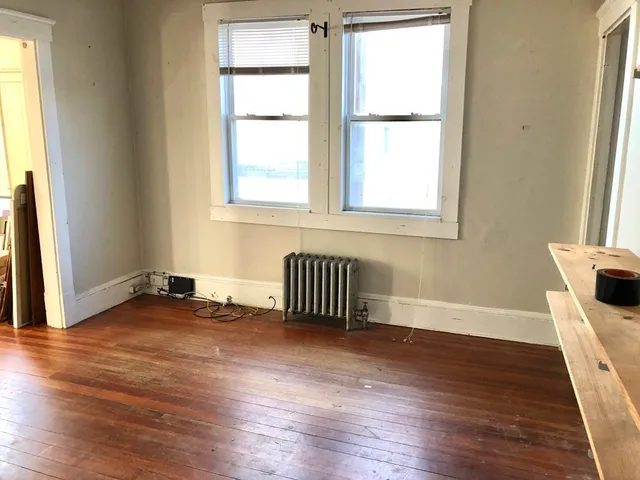 a view of an empty room with wooden floor and a window
