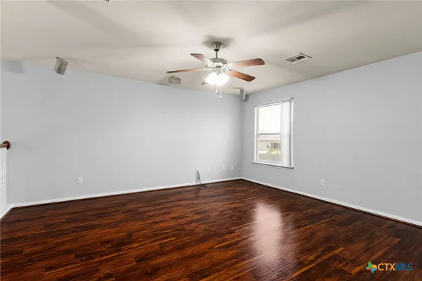 a view of an empty room with wooden floor and a ceiling fan