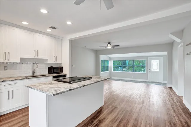 a kitchen with granite countertop a stove a sink a refrigerator and white cabinets with wooden floor