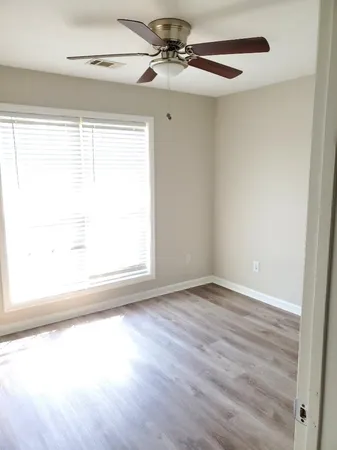 an empty room with wooden floor fan and windows