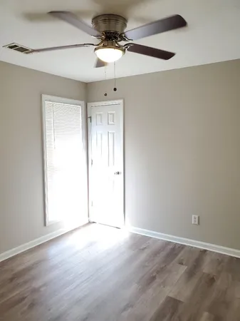 an empty room with wooden floor chandelier fan and windows