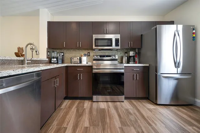 a kitchen with stainless steel appliances granite countertop a refrigerator stove a sink and dishwasher with wooden floor