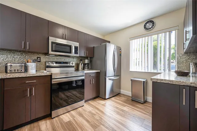 a kitchen with stainless steel appliances granite countertop a stove a sink dishwasher a refrigerator and a microwave oven with wooden floor