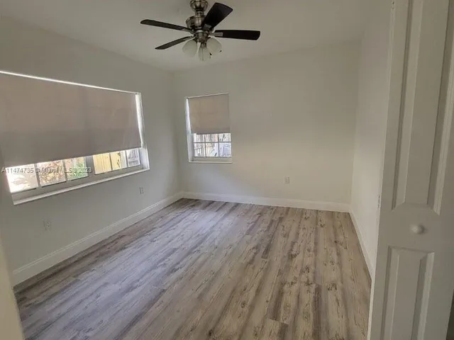 an empty room with wooden floor fan and windows