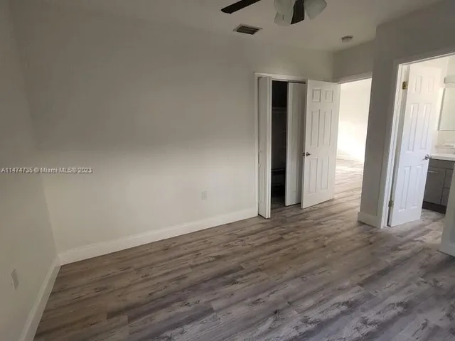 a view of an empty room with wooden floor and a ceiling fan