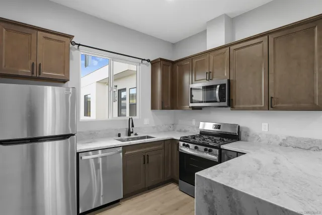 a kitchen with stainless steel appliances granite countertop a dining table chairs refrigerator and microwave