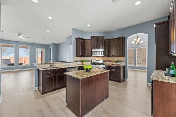 a kitchen with stainless steel appliances granite countertop a stove top oven a sink dishwasher a dining table and chairs with wooden floors