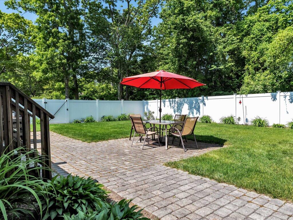 1309 Shootflying Hill Road Centerville, MA 02632 - Photo 37 of 52 a view of a patio with chairs and a table and chairs under an umbrella