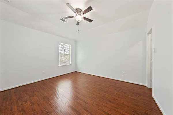 an empty room with wooden floor ceiling fan and window