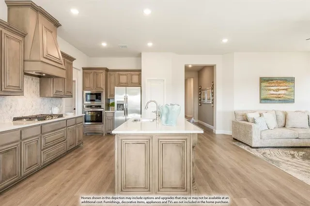 a large white kitchen with granite countertop a stove a sink a refrigerator and white cabinets with wooden floor