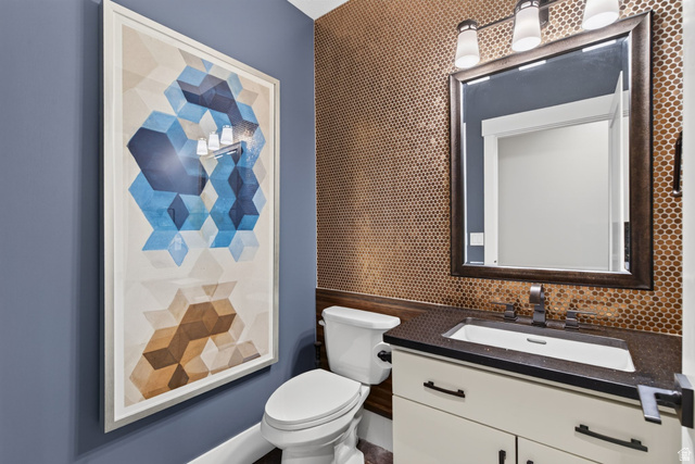 12308 Mariah Circle Draper, UT 84020 - Photo 95 of 293 Powder room featuring a hexagon tile accent wall, dark framed mirror with three-bulb vanity lighting, white vanity with dark countertop, and an undermount sink with a dark faucet