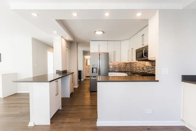 a large white kitchen with stainless steel appliances kitchen island granite countertop a refrigerator and a stove