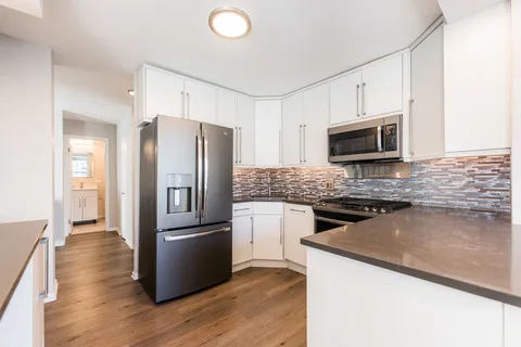 a kitchen with granite countertop a refrigerator a microwave a sink and dishwasher with wooden floor