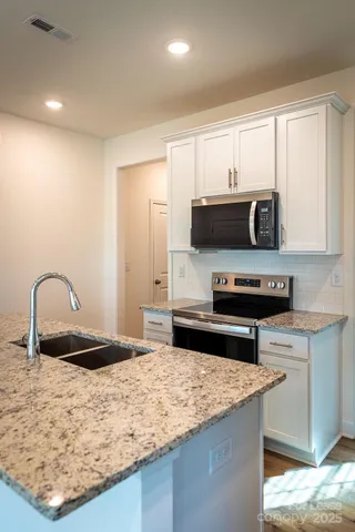 a living room with stainless steel appliances kitchen island granite countertop a rug a stove and a microwave