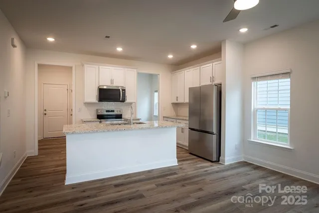 a kitchen with stainless steel appliances granite countertop a refrigerator a sink a stove a microwave and wooden floor