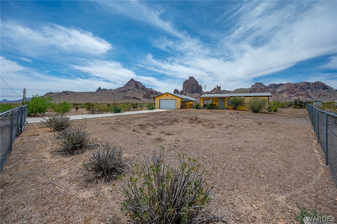 2465 Egar Road Golden Valley, AZ 86413 - Photo 75 of 98 The property features a single-story residence with a detached garage, both painted yellow, set against a backdrop of mountainous terrain