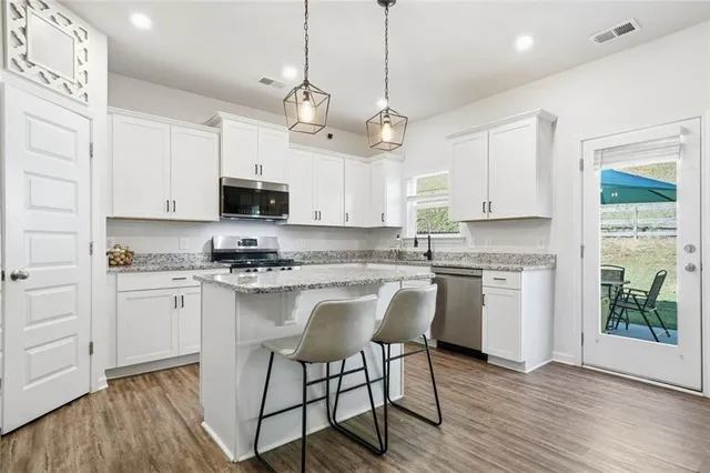 a kitchen with stainless steel appliances granite countertop a refrigerator a stove top oven a sink dishwasher a refrigerator and white cabinets with wooden floor