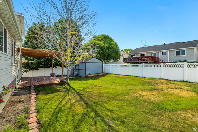5529 Ridge Hollow Way Kearns, UT 84118 - Photo 23 of 23 Expansive backyard featuring a wood-finish deck with a pergola, a storage shed, a white lattice fence, and a brick-edged planting bed