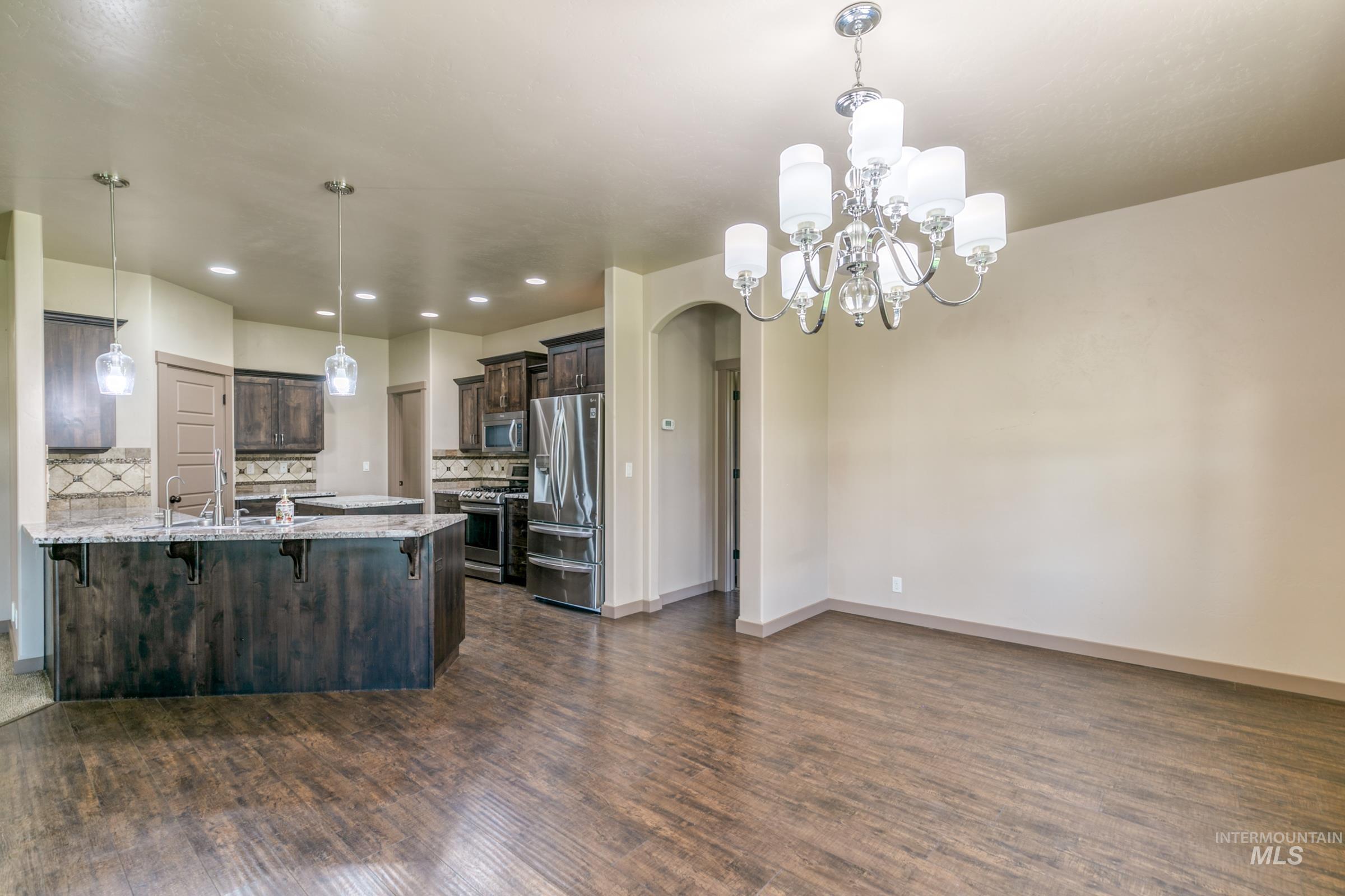 4316 Middlesboro Way Caldwell, ID 83607 - Photo 11 of 33 Open-concept layout featuring wood-finish flooring, a kitchen island with pendant lighting, stone countertops, and stainless steel appliances