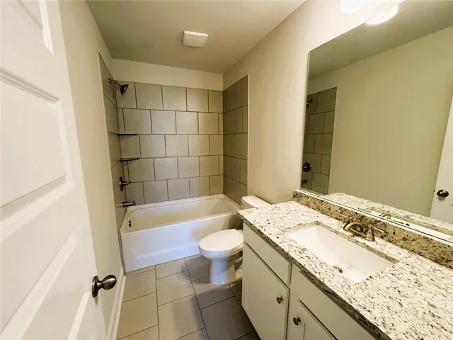 a bathroom with a granite countertop sink a toilet a mirror a bathtub and shower